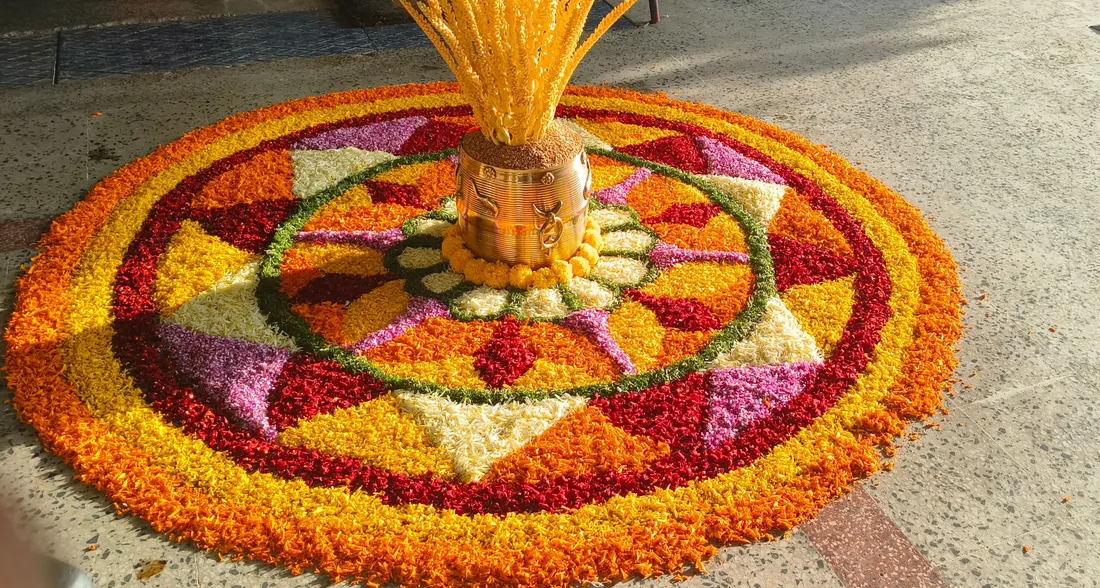 An Onam pookalam of marigold and coloured flowers laid around a brass nirapara filled with paddy, the flower carpet Kerala families lay at the threshold