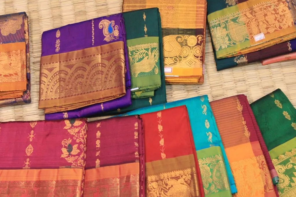 Folded Kanchipuram silk sarees in purple, teal and magenta with gold zari borders, woven on the handlooms of the Tamil land