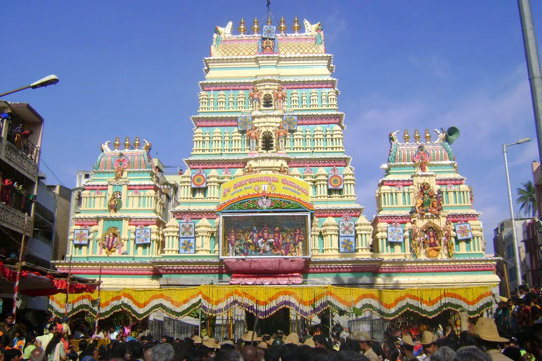 The painted gopuram of the Sri Dharmaraya Swamy temple at Thigalarapete, Bengaluru, its Kannada signboard naming the temple and the pete, with the Pandavas and Draupadi in the panel below and marigold garlands hung across the front