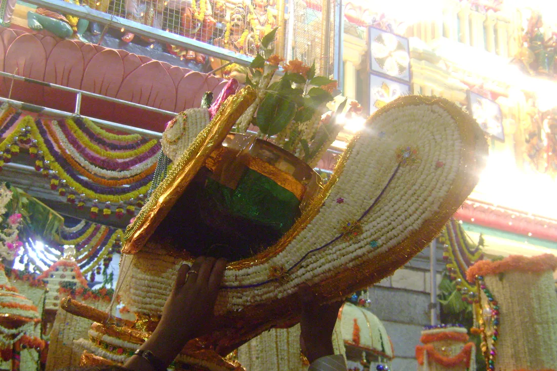 A tall lamp worked all over in strung jasmine and edged in gold, raised on its pole at the Bengaluru Karaga, with garlands of jasmine and marigold hung behind it