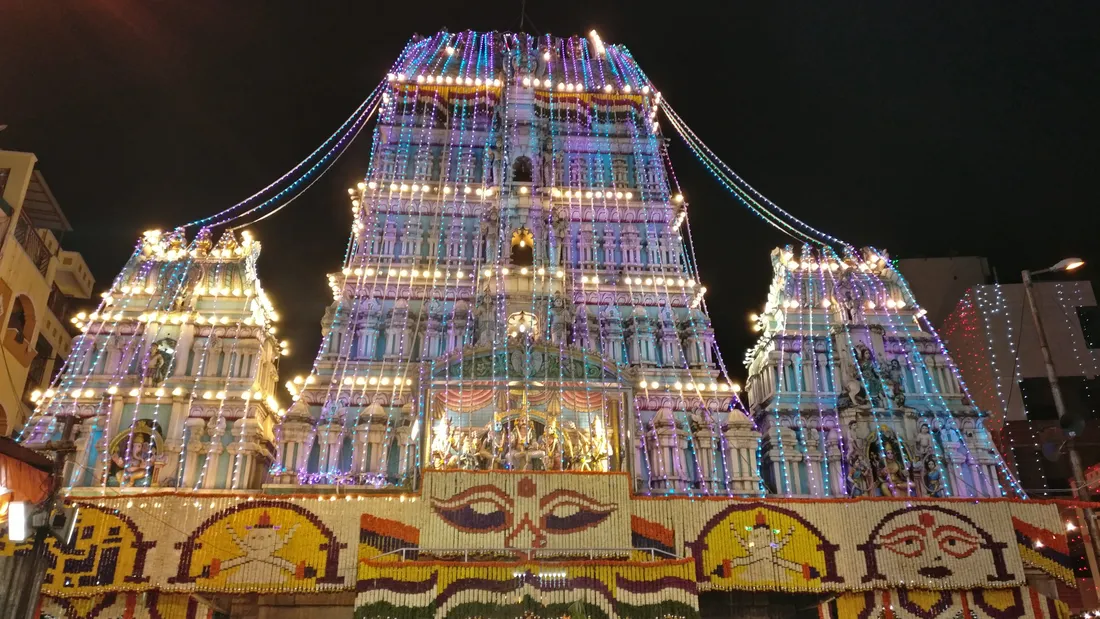 The Sri Dharmaraya Swamy temple at Thigalarapete lit for the Bengaluru Karaga at night, its whole front worked in strings of marigold and jasmine and hung with lights